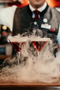 Zwei Cocktails mit Trockeneisnebel stehen an der Bar, dahinter ist ein Barkeeper im Hotel zu sehen.