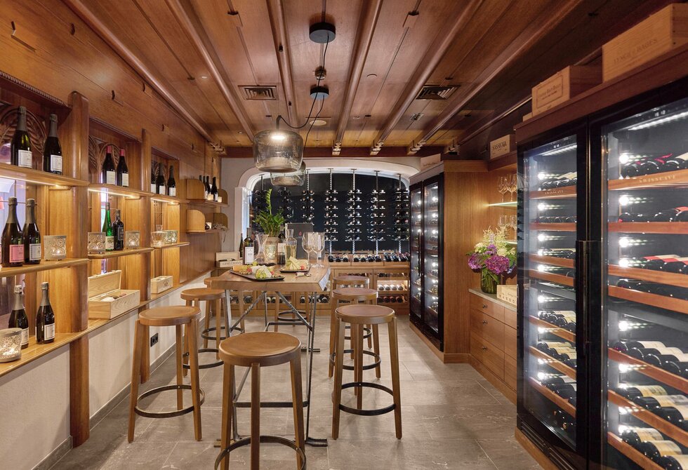 Ein holzverkleideter Weinkeller mit Stehtischen, Hockern, Weinregalen und beidseitigen Weinschränken.