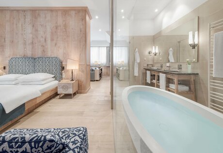 Ein helles Hotelzimmer mit getrenntem Schlafbereich und Bad mit freistehender Badewanne.