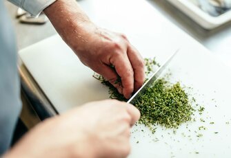 Eine Hand hackt frische Kräuter auf einem Schneidebrett in der Küche.
