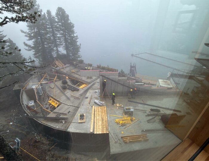 Auf der Baustelle am Hotel Hochschober sind Dachflächen, Gerüste und Baumaterialien im Nebel zu sehen.