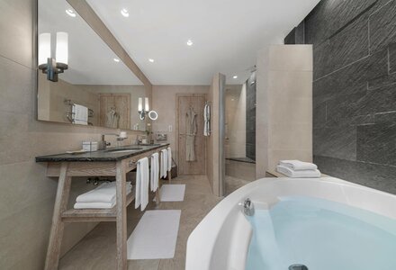 Ein modernes Badezimmer mit freistehender Badewanne, Doppelwaschbecken und dunkler Steinwand.