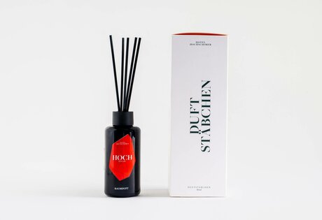A black fragrance bottle with reed sticks stands next to a white box labeled scented sticks.