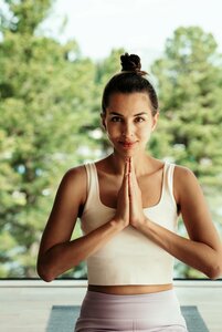 Eine Frau steht in gebetshaltung vor grüner Kulisse im Wellnessbereich.