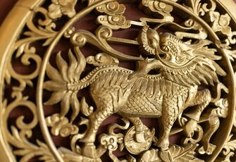 Eine goldene Drachenfigur aus Schnitzwerk ist vor filigranen Verzierungen im Chinaturm zu sehen.