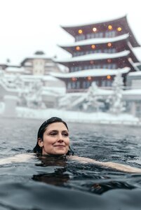 Eine Frau schwimmt im dunklen See-Bad vor dem verschneiten Chinaturm des Hotel Hochschober.