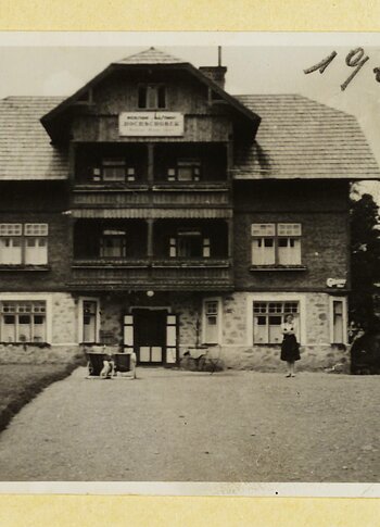 A historic multi-storey hotel building with a hipped roof and entrance is shown in an old photo from 1929.