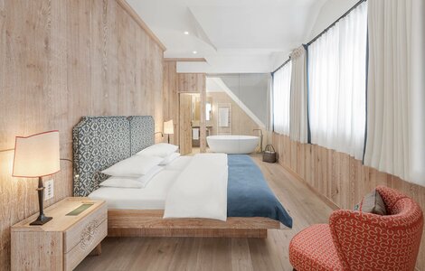 Ein helles Hotelzimmer mit Doppelbett, freistehender Badewanne und großen Fenstern im Hotel Hochschober.