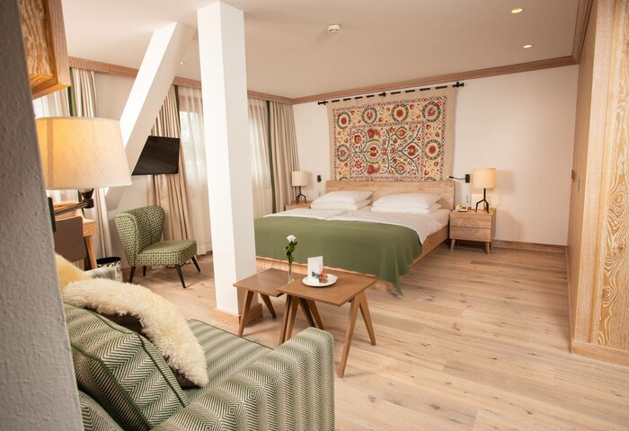 Comfort double room in the main building A comfort double room with a bed, green sofa, wooden tables and a wall hanging in Hotel Hochschober.