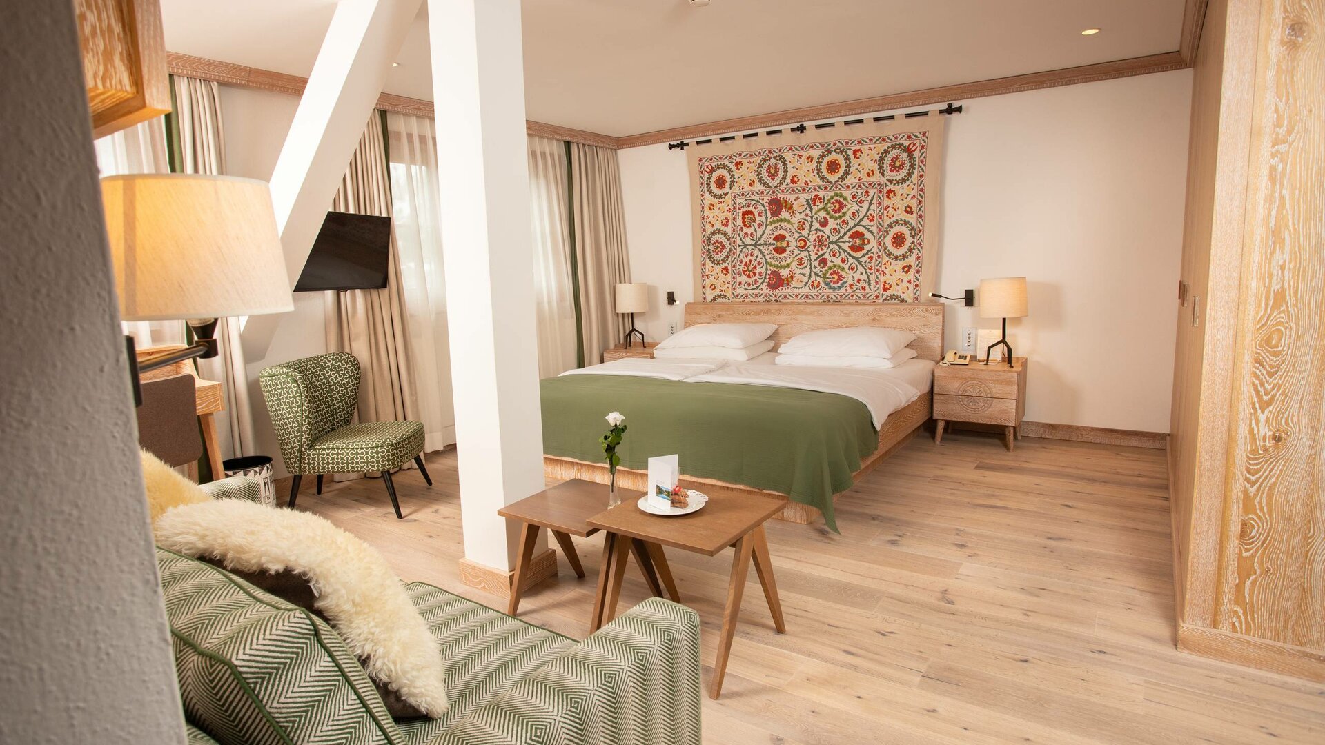 A comfort double room with a bed, green sofa, wooden tables and a wall hanging in Hotel Hochschober.