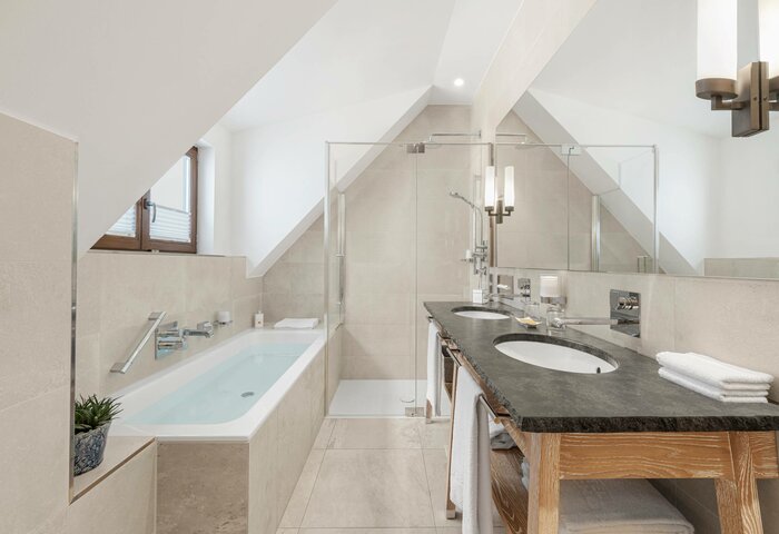 The Bergkristall family suite shows a bright bathroom with a bathtub, double sink and sloped ceiling.