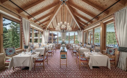 Ein helles Hotelrestaurant mit gedeckten Tischen, großen Fenstern und Blick auf den See.