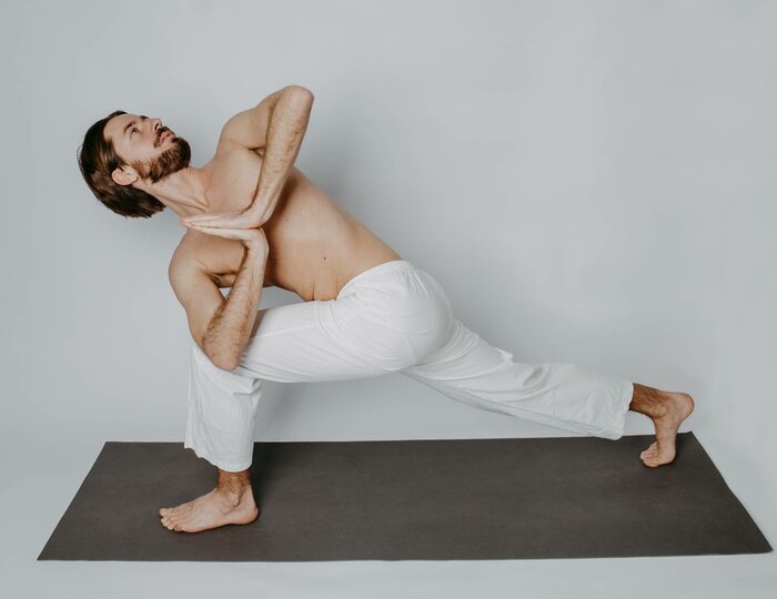 A man holds an intense yoga pose on a yoga mat against a plain light background.