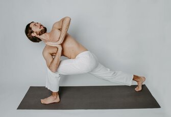 A man holds an intense yoga pose on a yoga mat against a plain light background.
