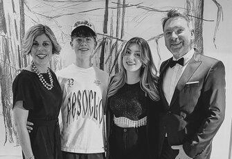 The Leeb and Klein host family stands together in front of a bright wall and smiles at the camera.