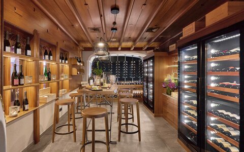 Ein Holzraum mit Barhockern, Weinregalen und einem beleuchteten Weinkühlschrank im Hotelrestaurant.