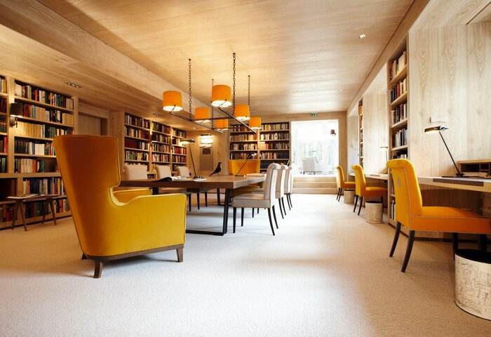 Eine gemütliche Hotelbibliothek mit Bücherregalen, Sesseln und einem großen Tisch im Hotel Hochschober.
