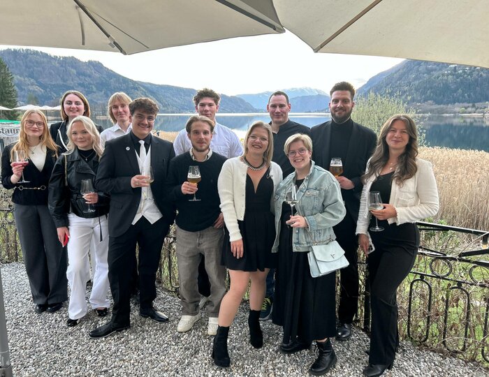 Eine Gruppe von Gästen posiert mit Getränken auf einer Terrasse vor Berg- und Seeblick im Hotel Hochschober.