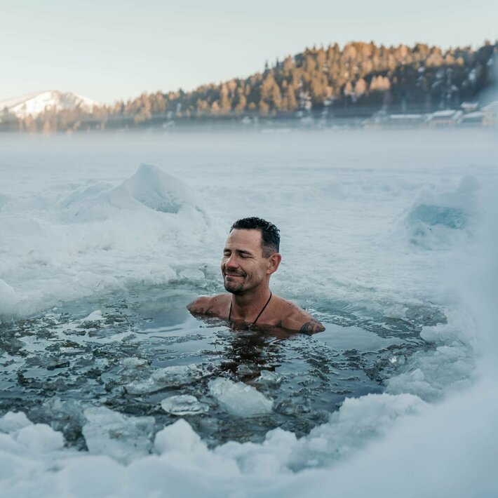 Ein Mann steht bis zur Brust im eisigen Wasser des beheizten See-Bads, umgeben von Schnee und Dunst.