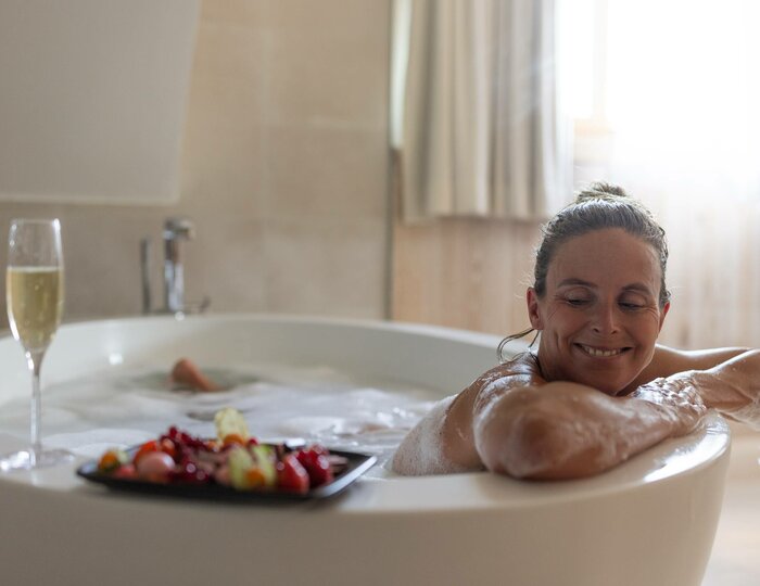 Badewanne mit Frühstück im Hotelzimmer Eine Frau entspannt in einer Badewanne mit einem Frühstücksgericht und einem Glas Sekt am Rand.