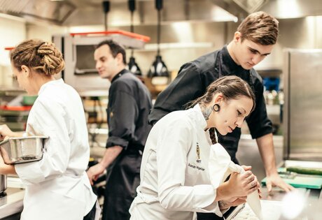 Mehrere Mitarbeitende arbeiten konzentriert in der Hotelküche und bereiten Zutaten gemeinsam vor.