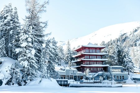 Der rote Chinaturm des Hotel Hochschober steht vor schneebedeckten Bäumen und Hängen am Seeufer.