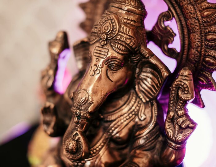 Eine bronzene Ganesha-Figur ist vor hellem Hintergrund mit violettem Licht zu sehen.