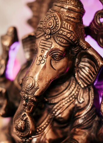 Eine bronzene Ganesha-Figur ist vor hellem Hintergrund mit violettem Licht zu sehen.