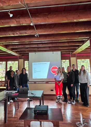 Praktikumsbetrieb: Gruppe bei Präsentation im Holzraum Eine Gruppe steht in einem Holzraum vor einer Projektionswand; auf dem Tisch liegen Laptop und Beamer.