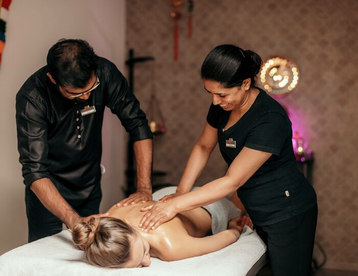 Zwei Therapeutinnen massieren eine Frau auf einer Liege in einem Spa-Raum.