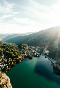 Luftaufnahme des Turracher Sees mit umliegenden Bergen, Wald und dem Ort am Ufer.
