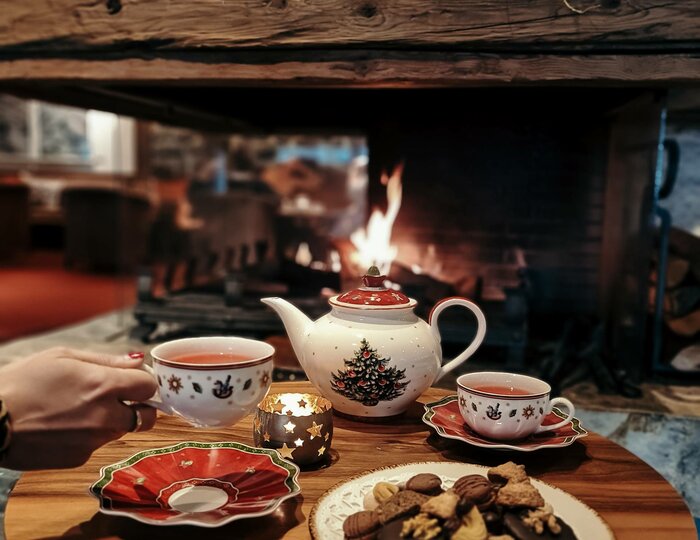 Advent-Zuckerl: Teetisch am Kamin im Hotel Hochschober Ein Teeservice mit Gebäck steht auf einem Holztisch vor dem brennenden Kamin.