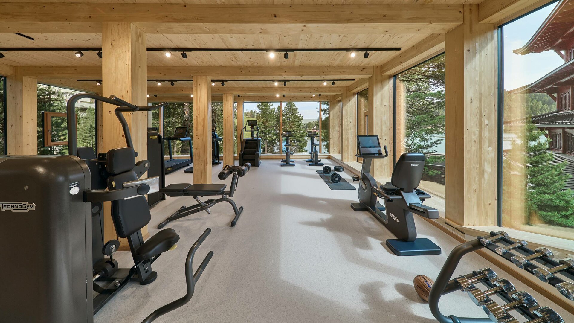 Ein heller Fitnessraum mit Trainingsgeräten, Hanteln und großen Fenstern im Hotel Hochschober.