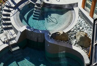 A heated lake pool with two water basins, steps and stone edging beside the building.