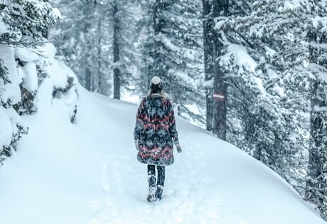 Eine Person wandert auf einem verschneiten Waldweg durch den Winter auf der Turracher Höhe.