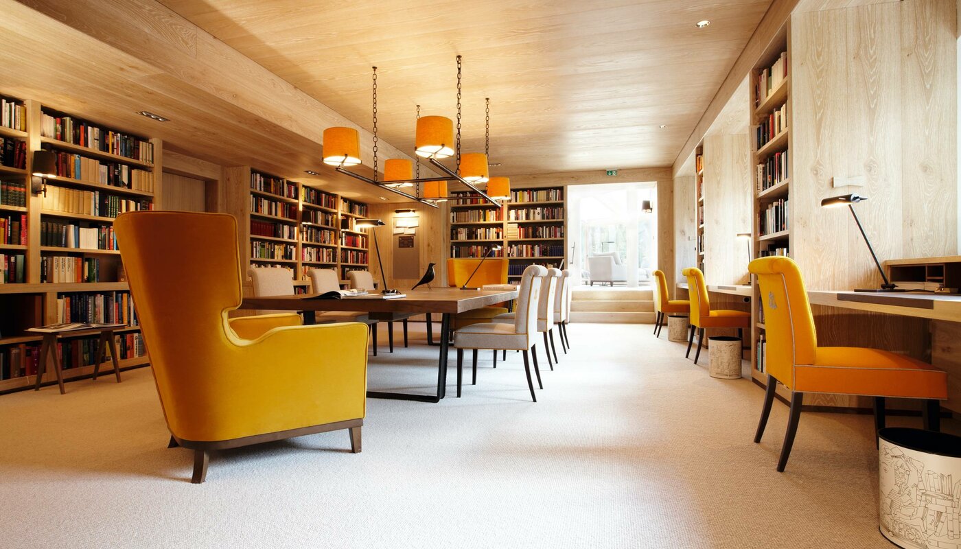 Eine gemütliche Hotelbibliothek mit Bücherregalen, Leseplätzen und gelben Sesseln im Hotel Hochschober.