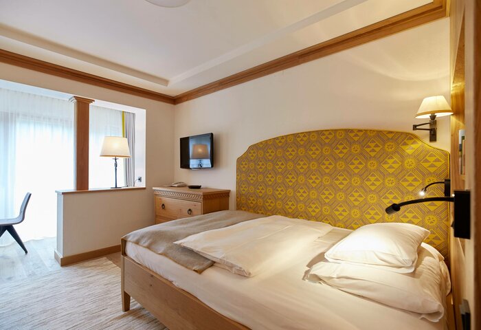 Single room at Hotel Hochschober A single room with a bed, yellow upholstered headboard, desk and view into a bright sitting area.