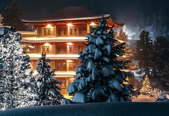 Das Hotel Hochschober leuchtet in der Nacht hinter verschneiten Tannen auf der Turracher Höhe.