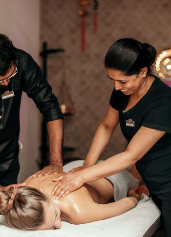 Zwei Spa-Mitarbeitende führen eine Abhyanga-Royal-Massage an einer liegenden Person im Kristall Spa durch.