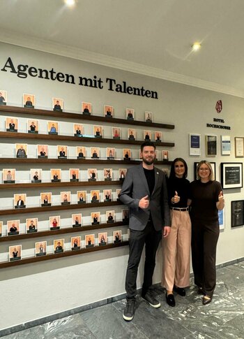 Mitarbeiterwand 2026 im Hotel Hochschober Drei Personen stehen vor einer Mitarbeiterwand mit vielen Porträtfotos im Hotel Hochschober.