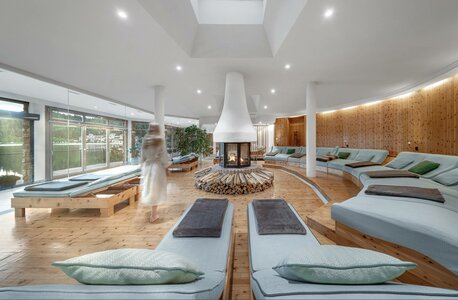 Ein heller Ruheraum mit Liegen, zentralem Kamin und großen Fenstern im Spa-Bereich des Hotel Hochschober.