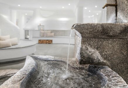 Eine Steinkaskade lässt Wasser in ein rundes Becken im hellen Wellnessbereich des Hotel Hochschober fließen.