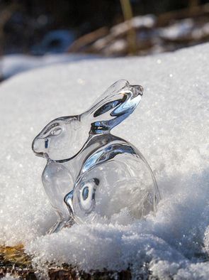 Ein Osterhase aus Glas steht auf einer schneebedeckten Stelle im Sonnenschein