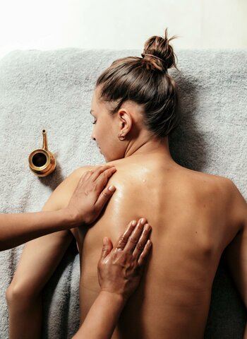 Eine Rückenmassage im Wellnessbereich mit einer liegenden Frau auf einem Handtuch.
