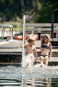 Zwei Kinder sitzen an der Beckenstufe im Pool und planschen im Wasser.