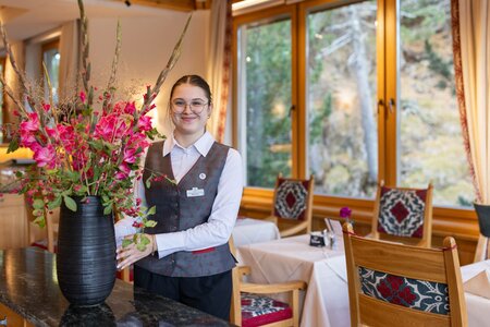 Eine Mitarbeiterin steht im Hotelrestaurant neben einer großen Vase mit Blumen.