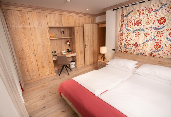 A bedroom in the family apartment shows a double bed, wooden built-in storage, a desk and a colorful wall textile.