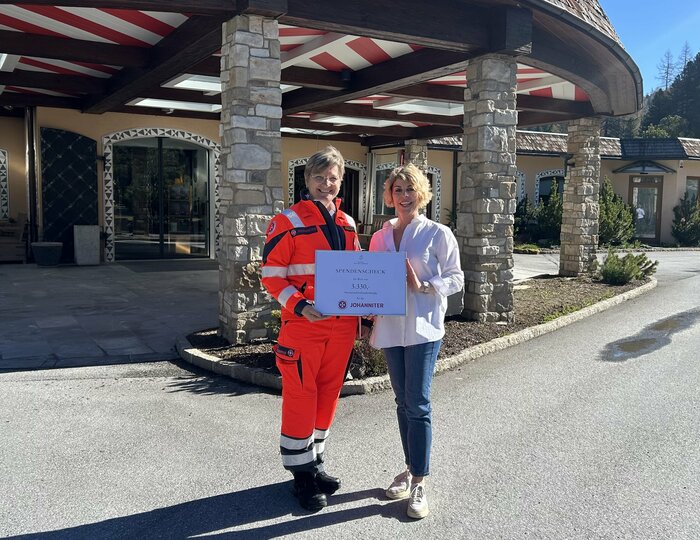 Eine Frau und ein Johanniter in Einsatzkleidung halten vor dem Hotel Hochschober ein Schild.