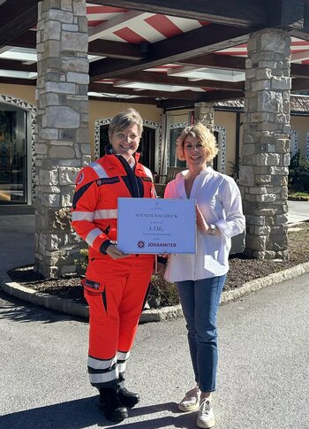 Johanniter vor dem Hotel Hochschober Eine Frau und ein Johanniter in Einsatzkleidung halten vor dem Hotel Hochschober ein Schild.