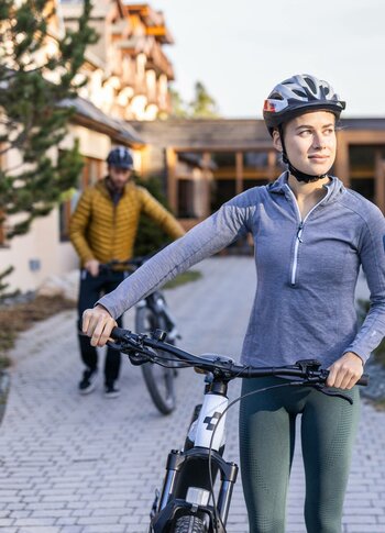E-Bike-Verleih im Hotel Hochschober Eine Frau mit Fahrradhelm steht mit einem E-Bike im Hotelhof, im Hintergrund schiebt ein Mann ein Rad.